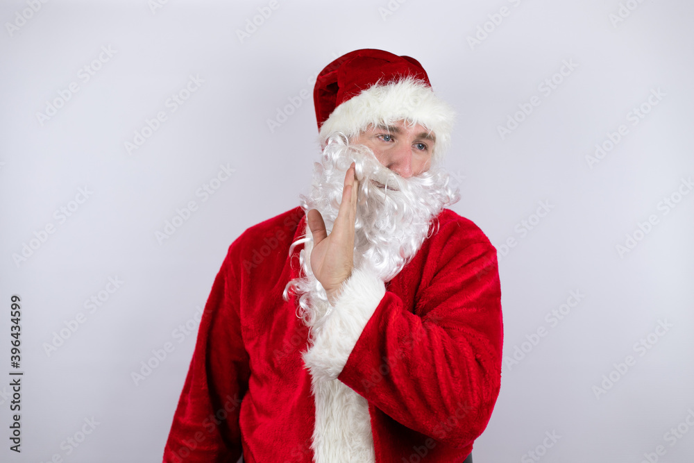Man dressed as Santa Claus standing over isolated white background with hand on mouth telling secret rumor, whispering malicious talk conversation Man dressed as Santa Claus standing over isolated white background with hand on mouth telling secret rumor, whispering malicious talk conversation