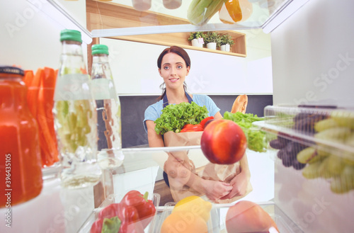 Portrait of female standing near open fridge full of healthy food  vegetables and fruits. Portrait of female