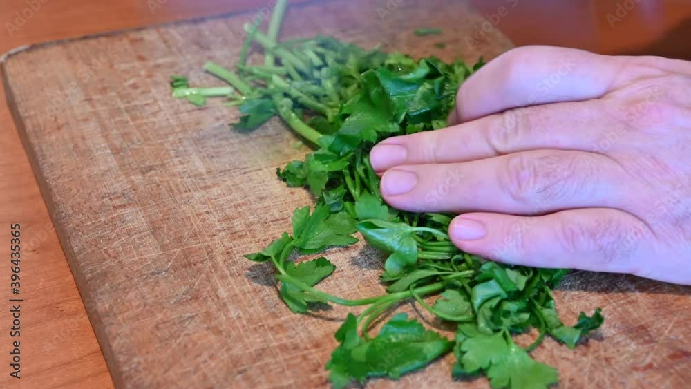 Scenes of life at home: in the kitchen preparing the chopped parsley on the cutting board. With a quick movement of the knife,the blade chops the parsley leaves finely.The hand holds the leaves still Scenes of life at home: in the kitchen preparing the chopped parsley on the cutting board. With a quick movement of the knife,the blade chops the parsley leaves finely.The hand holds the leaves still