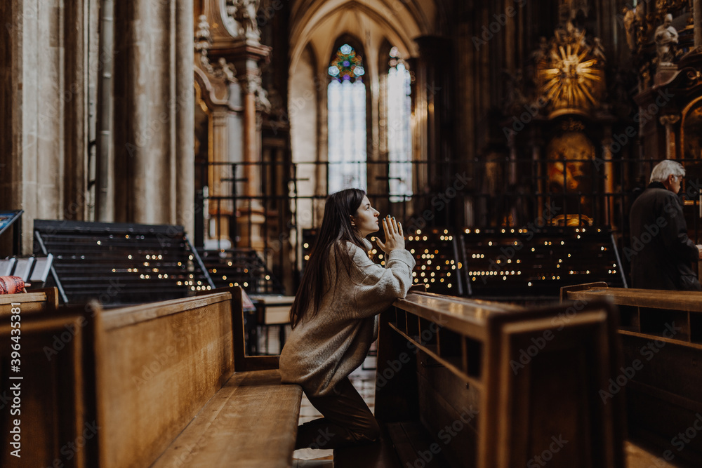 a young pretty woman came to the temple to pray to God. The parishioner of the church sits on a bench with her hands folded for prayer and heartily prays. copy space