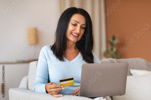 Woman making purchases using laptop holding card