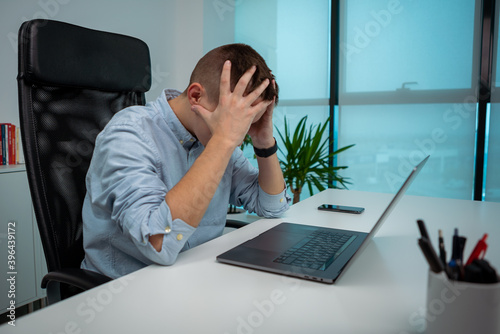 Tired or stressed young businessman sitting in front of computer in office. photo