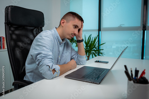 Tired or stressed young businessman sitting in front of computer in office. photo
