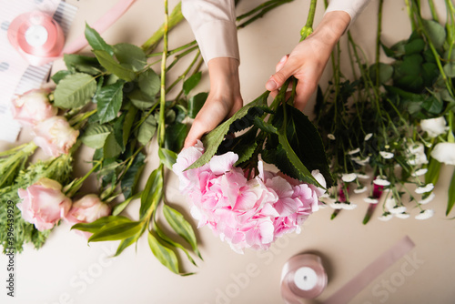 Cropped view of florist holding blooming hydrangea, while composing bouquets near flowers and decorative ribbons on desk
