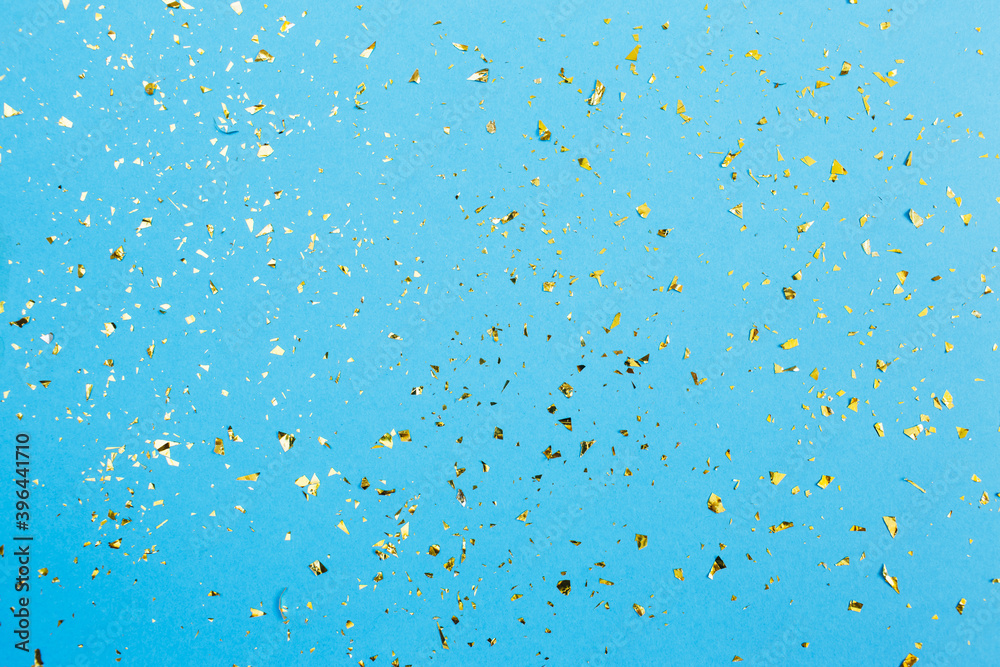 Golden confetti on blue paper background. Festive holiday backdrop. Birthday congratulations Christmas New Year. Flat lay, top view, copy space.