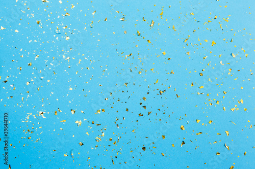 Golden confetti on blue paper background. Festive holiday backdrop. Birthday congratulations Christmas New Year. Flat lay, top view, copy space.