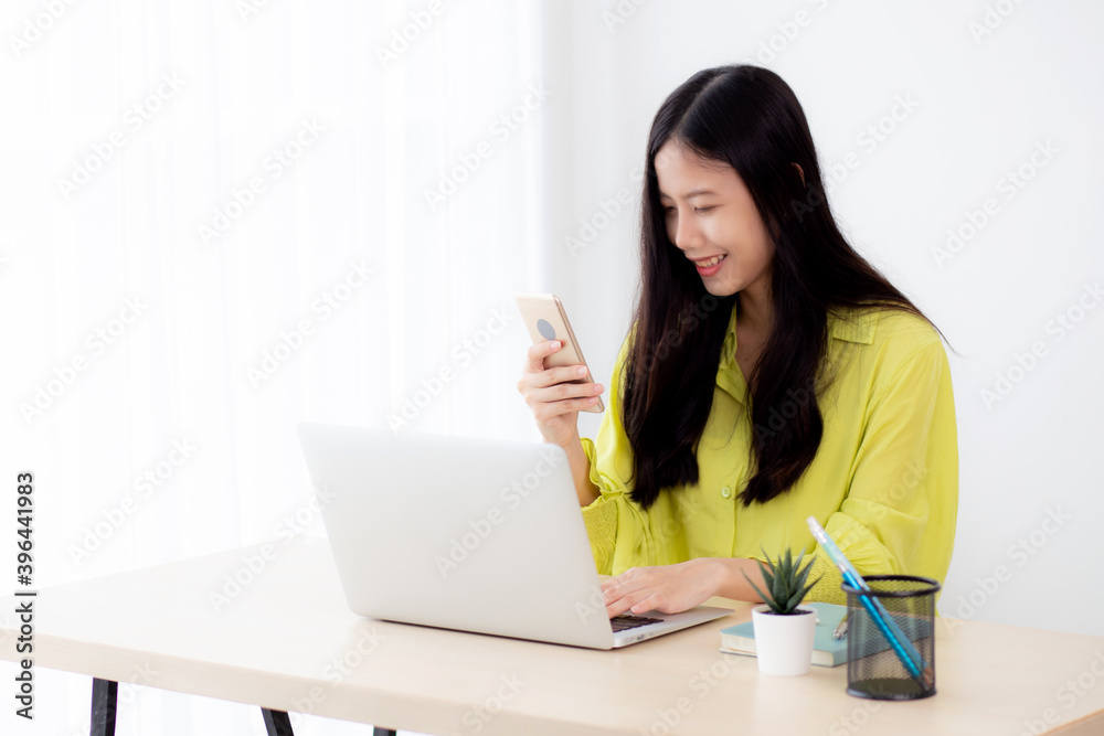 Young asian businesswoman working on laptop computer online on desk at home office, freelance woman looking message on smart phone and typing on notebook on table, business and communication concept. Young asian businesswoman working on laptop computer online on desk at home office, freelance woman looking message on smart phone and typing on notebook on table, business and communication concept.