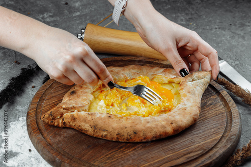 close-up of female hands with a knife and a fork mix the egg cheese in Adjarian khachapuri on a plate in a restaurant. Georgian national food photo