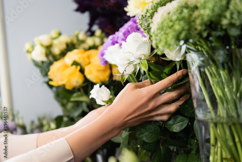 Cropped view of female florist caring about white roses on rack of flowers in store on blurred background