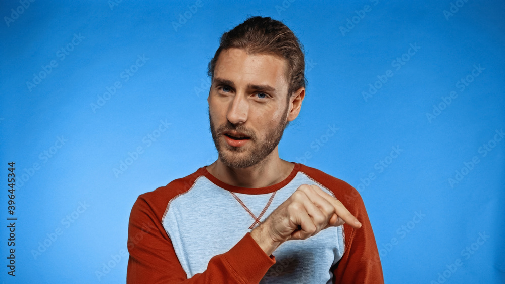 young bearded man pointing with finger and looking at camera on blue