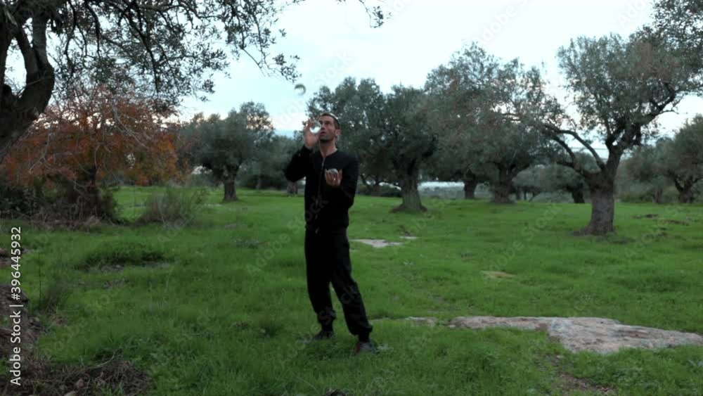 Professional juggler performing tricks with 3 transparent balls. Slow motion wide angle shot with olive trees in the background. Professional juggler performing tricks with 3 transparent balls. Slow motion wide angle shot with olive trees in the background.