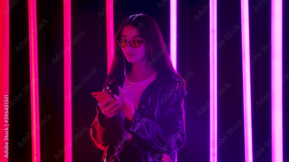 Portrait of a pretty young beautiful woman in stylish sunglasses is dancing and enjoying music from smartphone in white headphones. Slow motion. Portrait of a pretty young beautiful woman in stylish sunglasses is dancing and enjoying music from smartphone in white headphones. Slow motion.