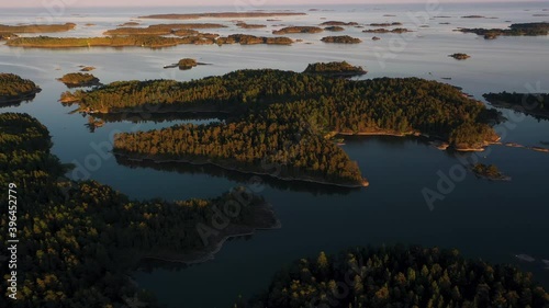 Aerial view away from sunlit, archipelago islands, warm, summer sunset, in the Swedish Archipelago, Sweden  - reverse, tilt up, drone shot photo