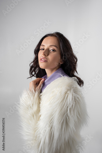  young woman in stylish white faux fur jacket posing on grey background