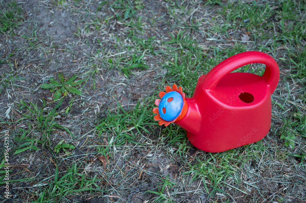 Red toy watering can in a garden