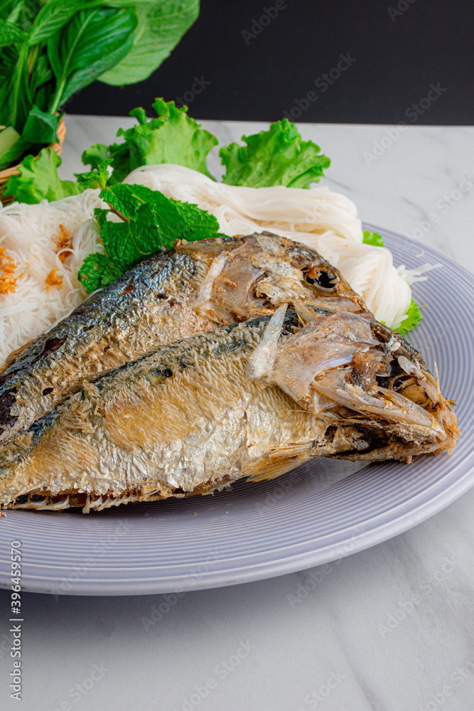 Fried two short bodied mackerel fishes and vegetable on white plate with black background.Close-up Fried two short bodied mackerel fishes and vegetable on white plate with black background.Close-up