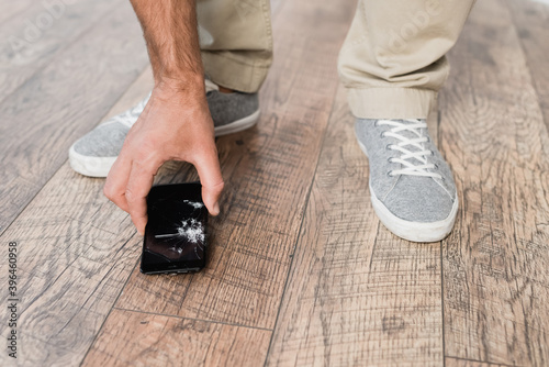 Cropped view of businessman taking smashed smartphone from floor