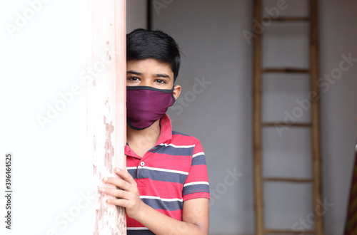 Portrait of young Indian boy wearing protective mask and watching out at home  