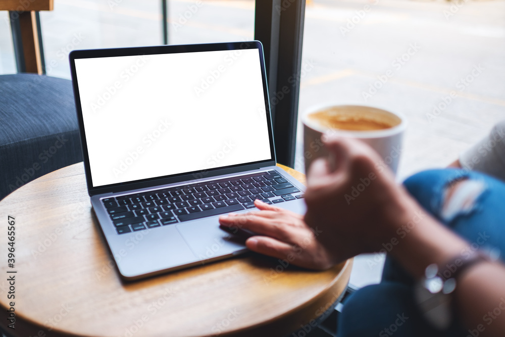 Mockup image of a woman touching on laptop computer touchpad with blank white desktop screen while drinking coffee Mockup image of a woman touching on laptop computer touchpad with blank white desktop screen while drinking coffee