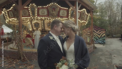 Push in on a couple with their foreheads together as they pose in front of a carousel photo