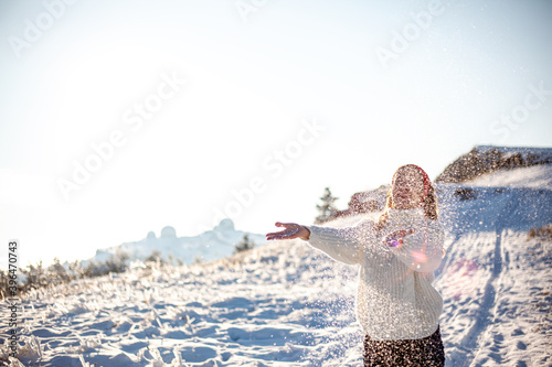 Beautiful woman in white oversize sweater and hat enjoing winter moments in snowy morning. Happy smiling lady covered in snow