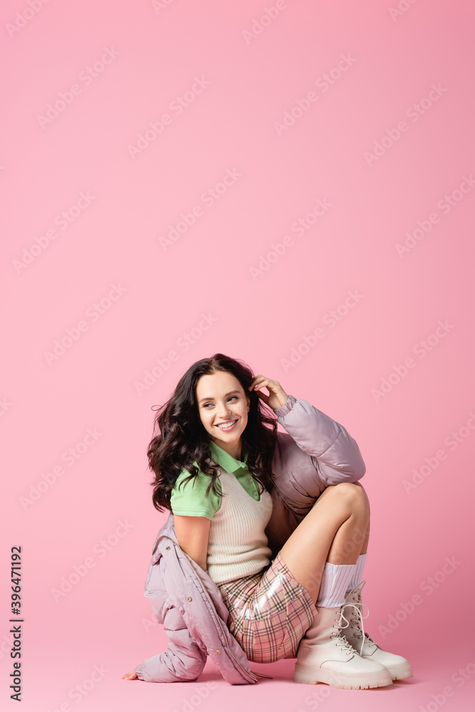 brunette young woman in stylish winter outfit posing on floor on pink background brunette young woman in stylish winter outfit posing on floor on pink background