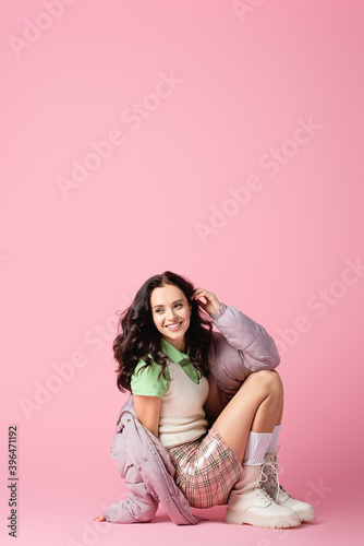  brunette young woman in stylish winter outfit posing on floor on pink background