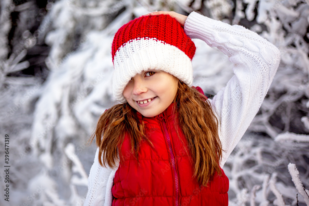 Happy girl playing with snow in frosty winter . Child dressed red christmas hat , red vest and white blouse, walking in the snowy nature Happy girl playing with snow in frosty winter . Child dressed red christmas hat , red vest and white blouse, walking in the snowy nature