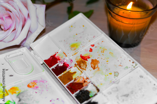 plastic palette with splashed watercolors, delicate creamy rose. concept of desktop of woman artist drawing lessons at home.
