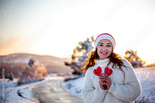 Portrait of beautiful woman holding the symbol of love a red heart in hands on valemtine day against the road to journey. Romantic day for female in snow nature.  photo