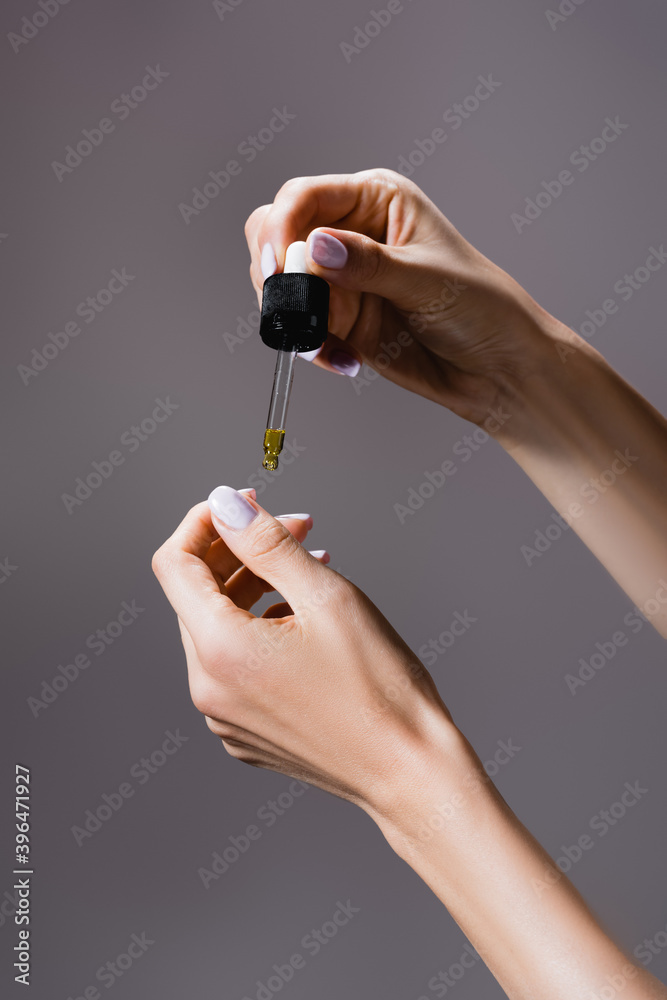 cropped view of woman applying oil from pipette on fingernails isolated on grey, stock image cropped view of woman applying oil from pipette on fingernails isolated on grey, stock image