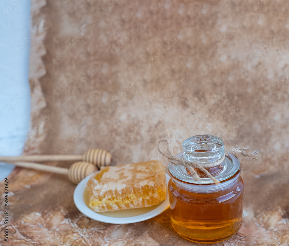 Fototapeta premium glass jar full of honey, plate with honeycomb on light brown background