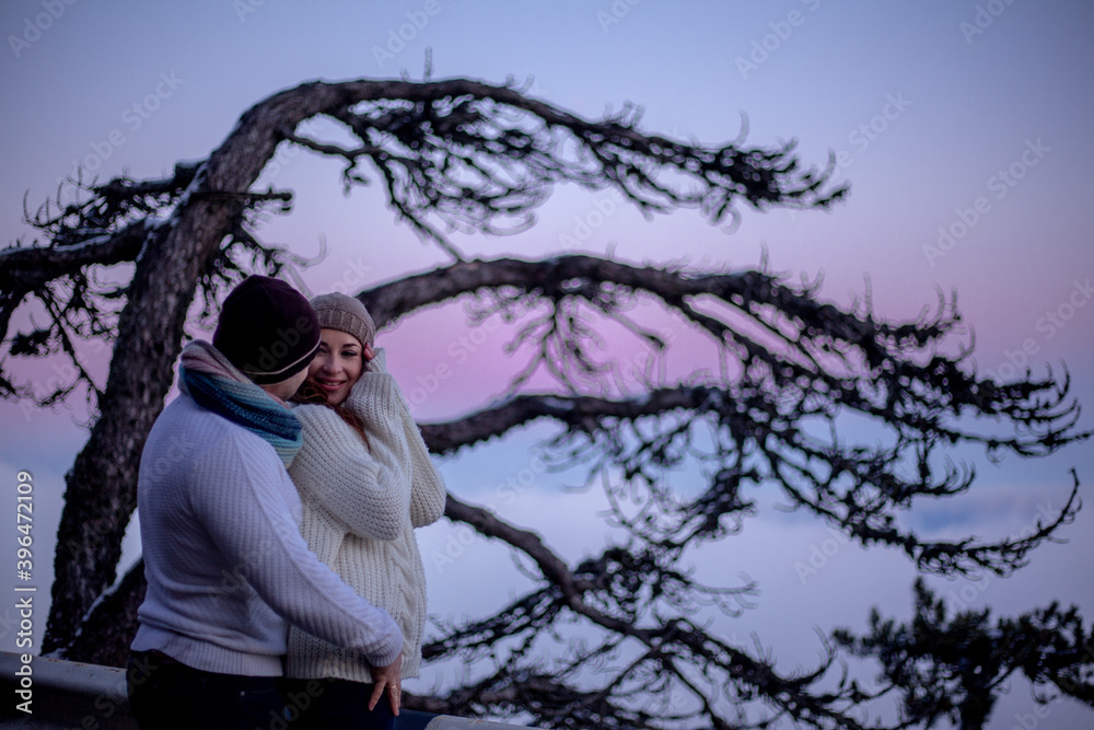 happy couple in sweaters hugging outdoor in snow day. The people above the clouds in the evening look at the blanket from the cloud happy couple in sweaters hugging outdoor in snow day. The people above the clouds in the evening look at the blanket from the cloud