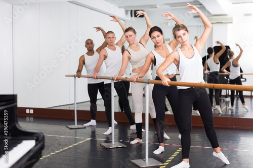 Group of people doing exercises using barre in gym with focus to fit athletic toned .woman in foreground in health and fitness concept