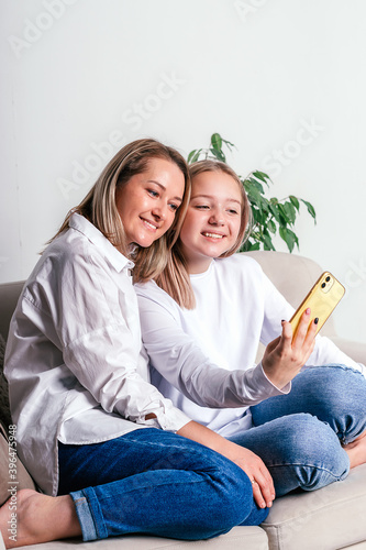 Mother with teenage daughter sitting at home on the couch and using smartphone.Video communication.Coronavirus pandemic,quarantine, self-isolation, socail distancing concept.