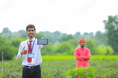 Young indian agronomist showing smart phone with farmer at green chilly field