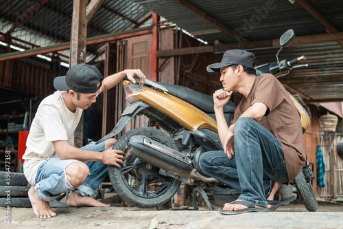 squatting male customer watching a squatting tire repairman checking a motorbike tire for a leak in a tire repair shop photo
