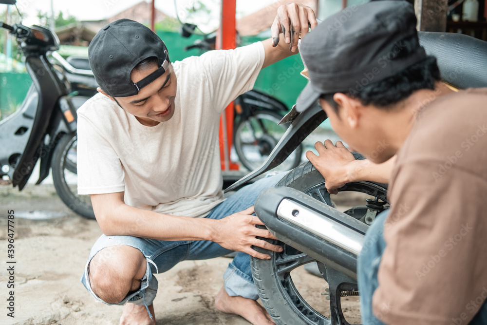 squatting male customer holding a tire while a squatting tire repairman checks a motorbike tire for a leak in a tire repair shop