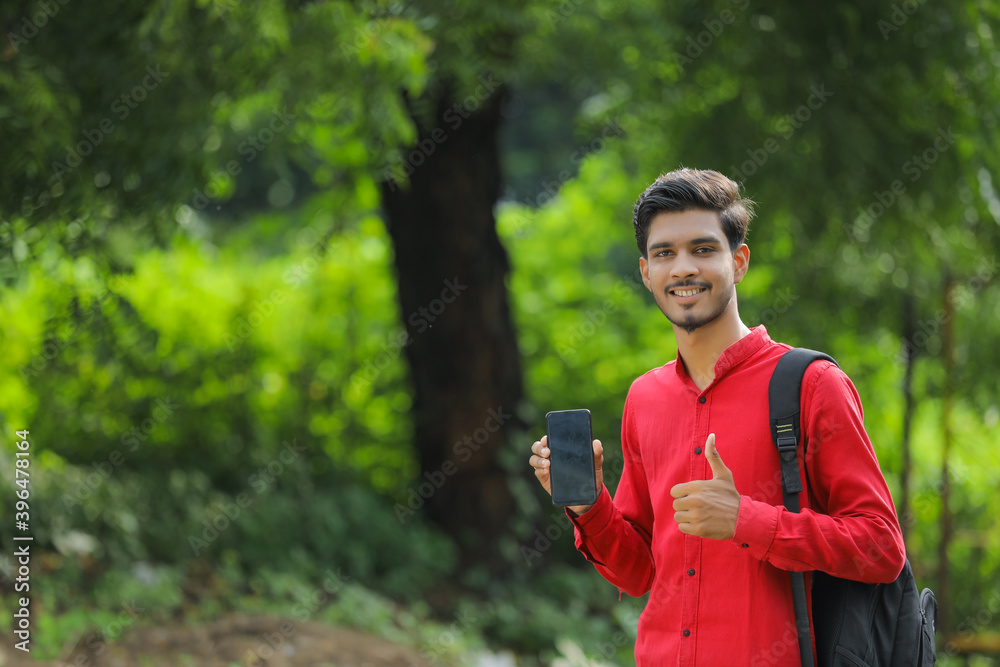 Young indian college student showing smart phone over nature background Young indian college student showing smart phone over nature background