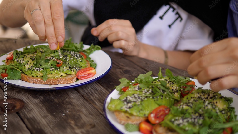 Two friends dress avocado toasts with lemon juice in cafe. Vegetarians dining out together 