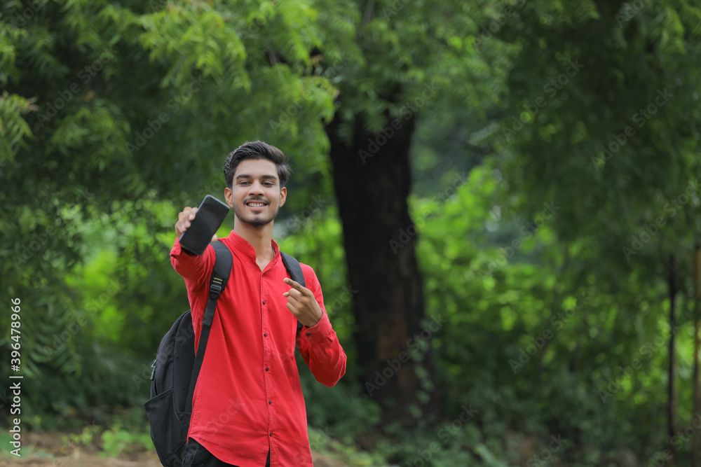 Young indian college student showing smart phone over nature background Young indian college student showing smart phone over nature background