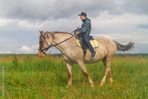 A teenage boy learns to ride a horse without stirrups. Learning to ride in the summer or autumn on the meadow. The child manages the horse independently. Training a teenager.