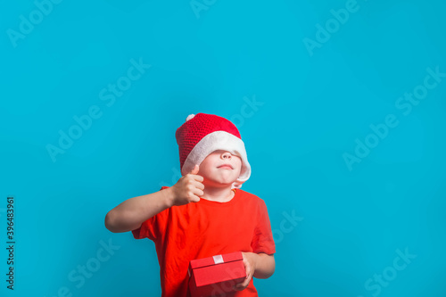 A child in a Christmas Santa Claus costume shows a like on a blue background in the Studio.