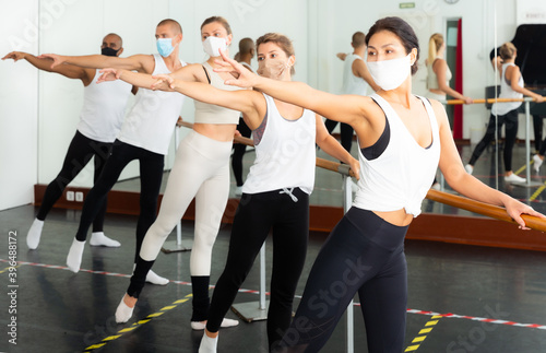 Group of people in masks doing exercises using barre in gym during coronavirus .pneumonia outbreak