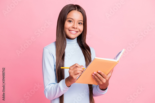 Portrait of attractive intellectual cheerful girl writing notes exercise book isolated over pink pastel color background