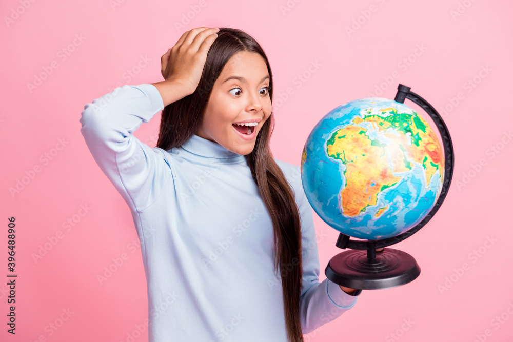 Close-up portrait of lovely cheerful amazed girl holding in hands globe learning countries lesson isolated over pink pastel color background Close-up portrait of lovely cheerful amazed girl holding in hands globe learning countries lesson isolated over pink pastel color background