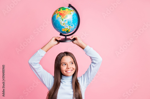 Portrait of attractive cheerful cute girl carrying globe on head learning world map copy space isolated over pink pastel color background © deagreez