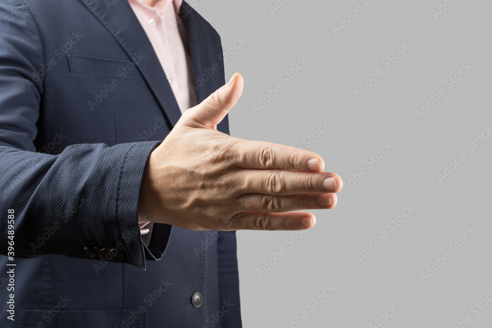 male businessman holds out his hand for a handshake on a gray background. Cropped, no head. Businessman and gesture concept