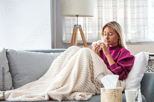 Cold And Flu. Portrait Of Ill Woman Caught Cold, Feeling Sick And Sneezing In Paper Wipe. Closeup Of Beautiful Unhealthy Girl Covered In Blanket Wiping Nose. Coronavirus, covid-19 photo