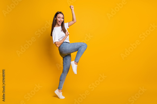 Photo portrait full body view of excited woman with raised fists on one leg celebrating isolated on vivid yellow colored background